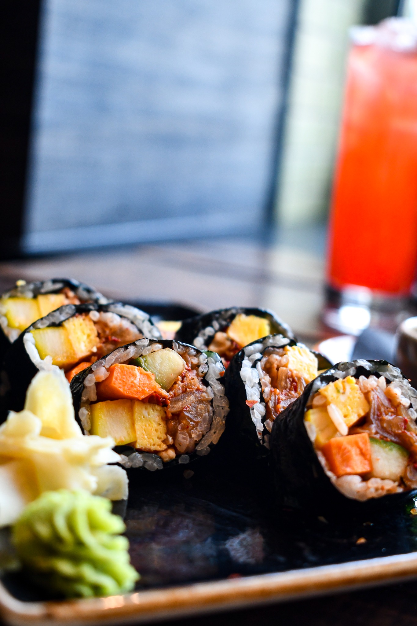 Modita sushi rolls with a cocktail softly blurred in the background
