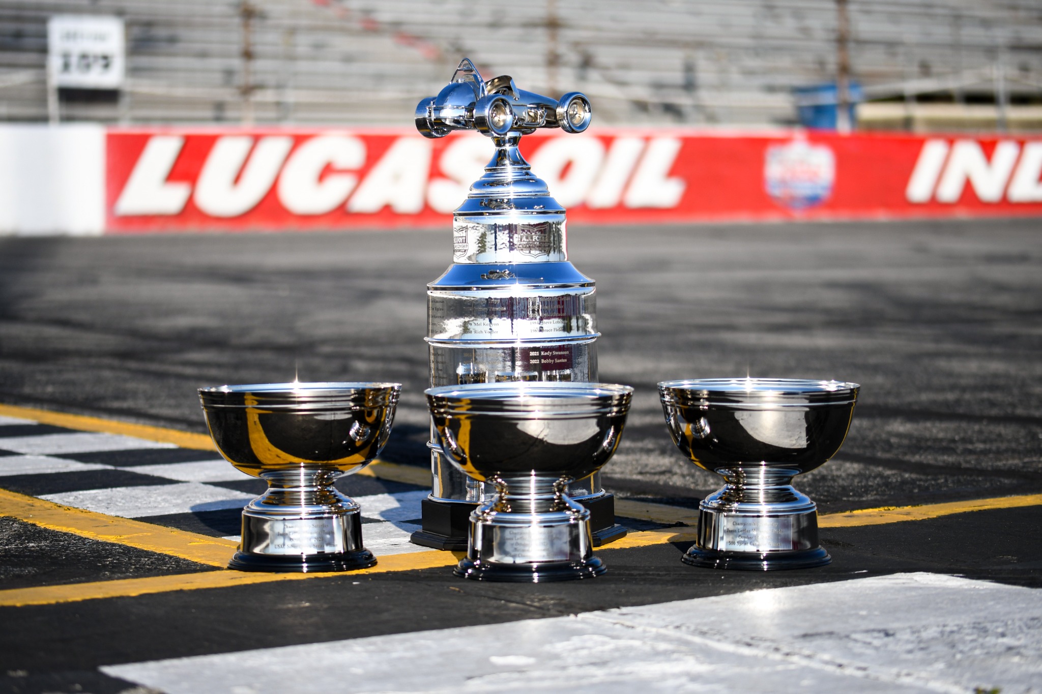 Championship trophy photographed on track with Lucas Oil branding in the background