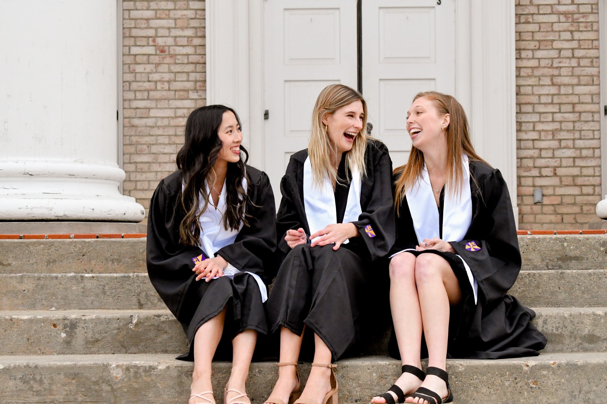 Three graduates laughing together on campus steps